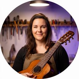 Lucía Alarcón sosteniendo una guitarra en el taller, con fondo de herramientas colgadas