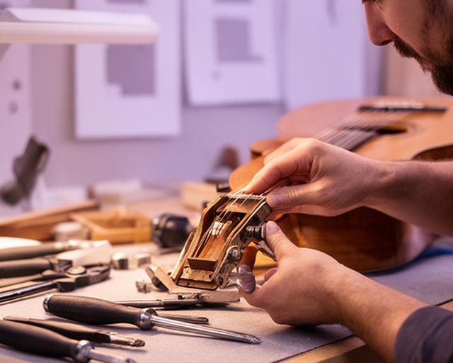Luthier revisando un instrumento de viento sobre una mesa de taller con planos y herramientas de precisión